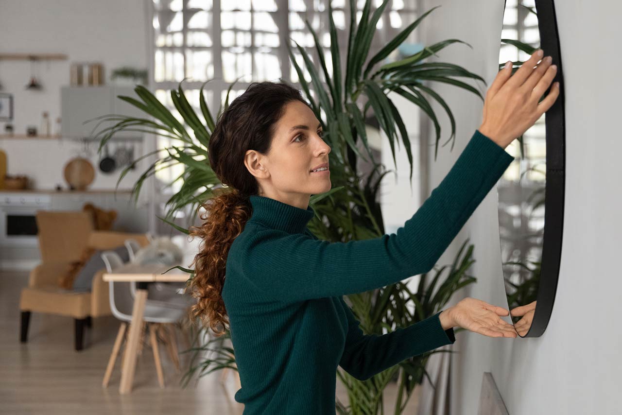 Close up smiling woman hanging or fixing mirror on wall