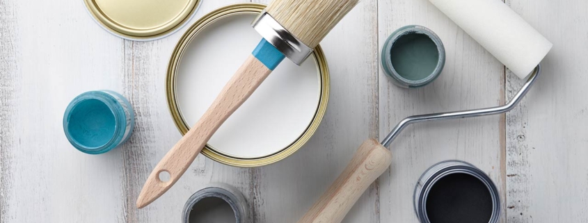 Paint brush, sponge roller, paints, waxes and other painting or decorating supplies on white wooden planks