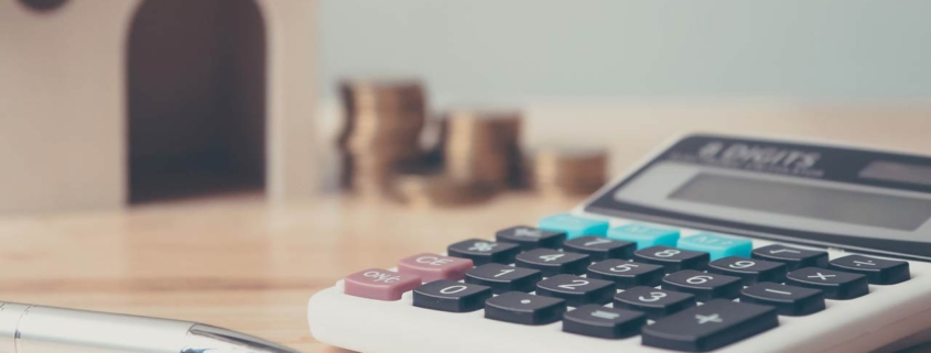 Calculator with wooden house and coins stack and pen on wood table