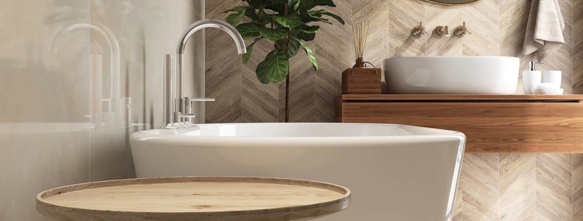 Round wooden side table, bathtub, fiddle leaf fig tree in luxury design bathroom in sunlight on beige brown tile wall