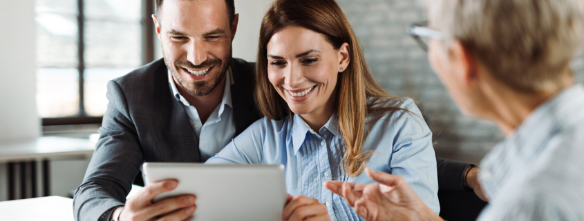 Happy couple using tablet while having a meeting with their real estate agent in the office